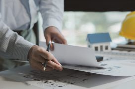 An engineer is studying blueprints to better understand the work to be done, An architect looks at building plans in his private office to understand the work assigned to him by his boss.